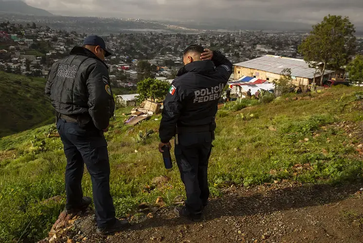 Mexico Federal Police officers talk near the border in East Tijuana during a tour with journalists. Just a short walk away is one of the few sections of the U.S.-Mexico border in Tijuana that has no fence. People sometimes cross the border here when seeking asylum or traveling with smugglers. Image by Erika Schultz. Mexico, 2019.