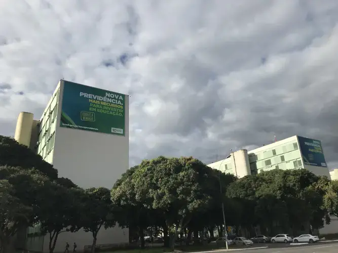 Government billboards at the top of each ministry building are promoting the benefits of approving a new social security system. The left billboard located atop the Education Ministry—where, in May, 2019, the federal education budget cuts were approved—reads 'The new social security. More resources to invest in education.' Image by Rafael Lima. Brazil, 2019. 