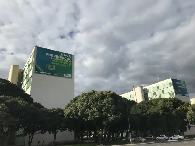 Government billboards at the top of each ministry building are promoting the benefits of approving a new social security system. The left billboard located atop the Education Ministry—where, in May, 2019, the federal education budget cuts were approved—reads 'The new social security. More resources to invest in education.' Image by Rafael Lima. Brazil, 2019.