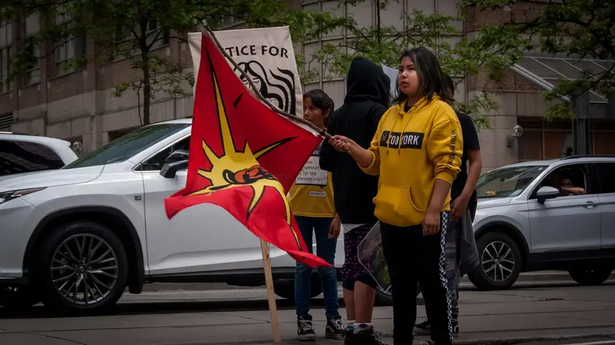 Jenae Turtle looks back at the marchers behind her, waving a Mohawk Warrior Flag often used to represent unity among Indigenous people. Canada, 2019. Image by Shelby Gilson.