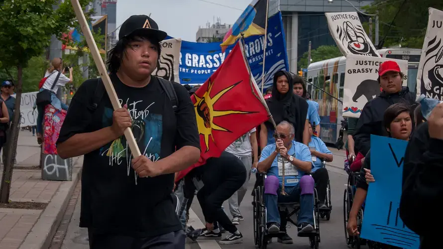 A Grassy Narrows youth, with a flag in his hand, helps to lead his community through the streets of Toronto. Canada, 2019. Image by Shelby Gilson.