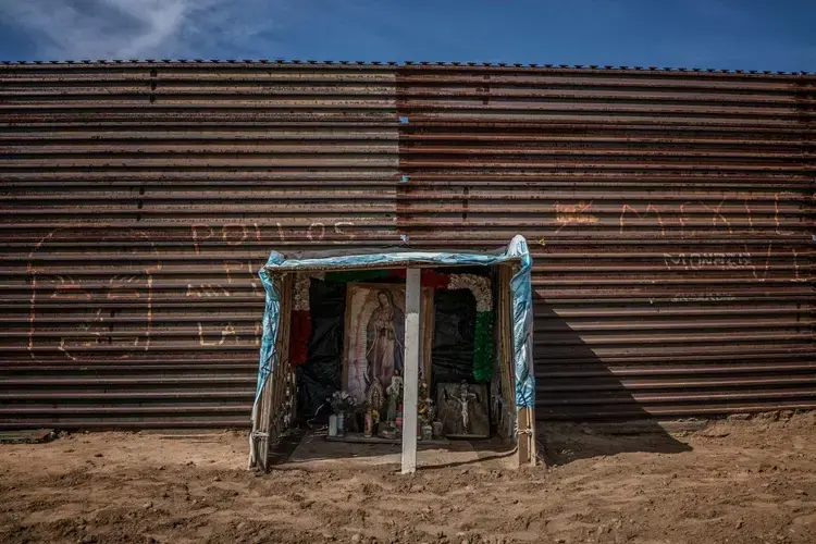 A Catholic shrine dedicated to the Virgin of Guadelupe is built right up against the U.S.-built border wall, by 'Luis', a deportee from the U.S. who lives on his hilltop redoubt above Playas de Tijuana, Baja California, Mexico. What he and other deportees fear most are 'coyote' traffickers or unknown migrants who prowl this hilltop either seeking to cross into the U.S. or who have more nefarious ambitions. Image by James Whitlow Delano. Mexico, 2017.