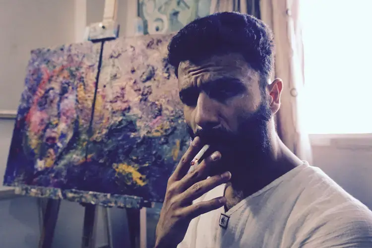 Emsallam Hdaib smokes a cigarette in his studio. Image by Aman Madan. Jordan, 2017.