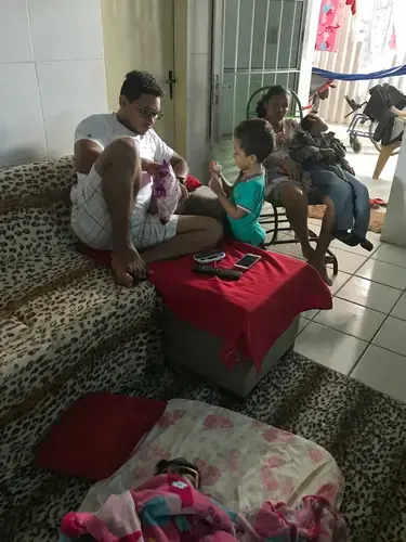 On a lazy Saturday morning at home, Jorge watches cartoons and eats marshmallows with his stepfather, Luiz Carlos Ribeiro Valadares Junior, while Valentina naps on a mattress near him and Dhulha cooks lunch for the family. Inspired by the cartoons, Jorge, who would rather be known as “Spiderman,” races around the house, shooting imaginary webs from his wrists. A neighbor from the community has stopped by with her ten-year-old son, who was born with microcephaly due to causes unrelated to Zika. In Dhulha’s municipality alone, there are 40 families with children with congenital Zika syndrome, and another 25 with children with microcephaly not associated with Zika. Image by Poonam Daryani. Brazil, 2017.