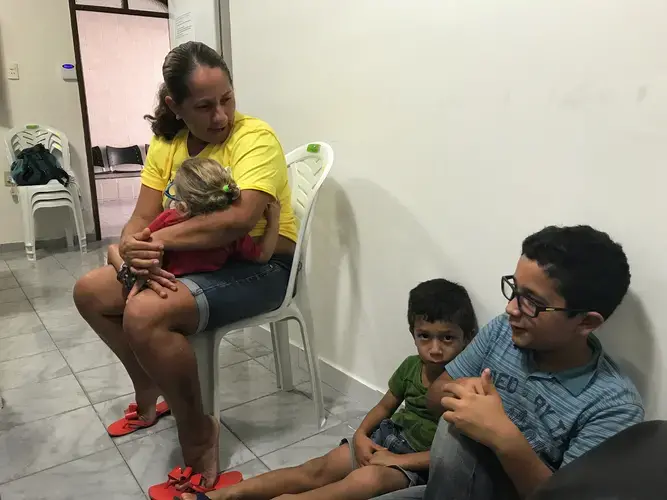 Josimary Gomes da Silva, 36, waits with three of her children for her son’s physical therapy appointment at a specialized microcephaly and congenital Zika syndrome clinic in Campina Grande, Paraíba. Her youngest son, Gilberto, was born with congenital Zika syndrome in 2015. With her at the IPESQ clinic are Marcos, 10, and Jorge, 6; her two oldest sons are teenagers and stayed home. “My ex-husband did not want to see Gilberto’s face, so I threw him out,” Josimary tells me. A single mom, she makes the 2.5 hour journey from her home to clinics and rehab centers in Campina Grande four times a week. Once a week, when Gilberto has a full day of appointments, Marcos and Jorge have to miss school to come with her into the city. This morning they left home at 5:40AM and will return after the sun sets. Image by Poonam Daryani. Brazil, 2017.