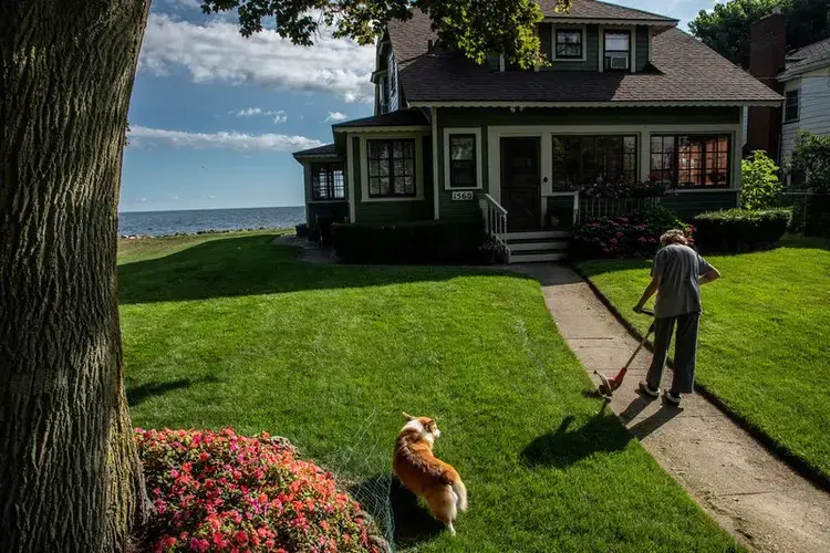 Nancy Sullivan, with dog Carter, tends to her house along the shore of Lake Ontario in Greece, New York, on July 30, 2020. She has lived at this house for the past 55 years and recently spent some of her retirement money to repair her seawall. Image by Zbigniew Bzdak/Chicago Tribune. United States, 2020.<br />