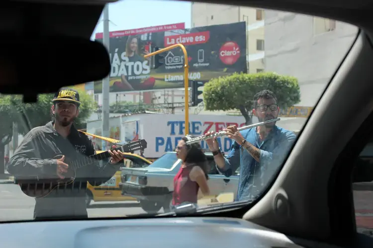 Venezuelans perform at a stoplight. One of them plays a popular Venezuelan instrument known for its four strings, a cuatro. Image by Mariana Rivas. Colombia, 2019.
