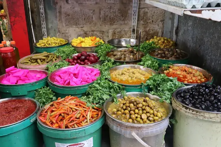 Classic dishes like falafel and hummus are served with pickled veggies to act as palate cleansers. Vegetables such as cauliflower, radish and eggplant steep in turmeric- and beet-infused solutions, which gives them these vibrant colors. A pickled delicacy is makdous, small eggplants cured in olive oil and stuffed with walnuts, garlic, and red pepper. Image by Carly Graf. Palestine, 2019.