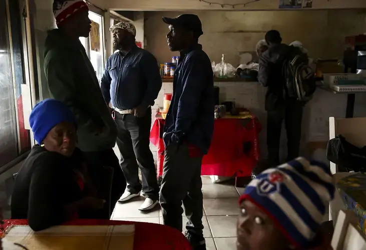 Jimmy Jeune, center, waits for his order in Wilthene Pierre’s Haitian restaurant in Tijuana. Pierre, an immigrant from Haiti, says his restaurant is known for barbecue, fried plantains and goat soup. Thousands of Haitians have migrated and settled in Tijuana in the past several years. Image by Erika Schultz. Mexico, 2019.