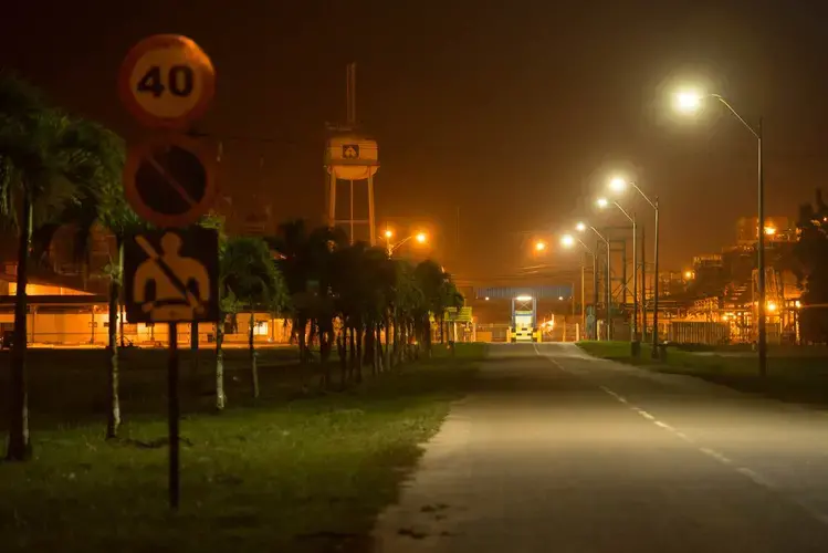 The sky at dusk is cut by the orange glow of the shuttered refinery at the Paranam Operations of Suralco, a subsidiary of Alcoa. Image by Stephanie Strasburg. Suriname, 2017.<br />
