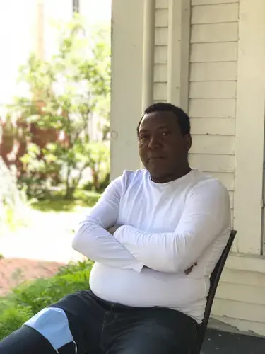 Panbo Boris sitting on the porch of his home in Yarmouth. Image by Francesca Bentley. United States, 2020.