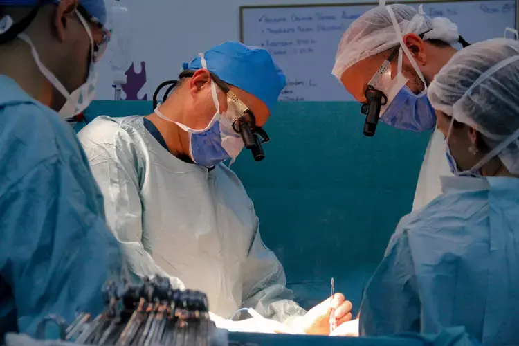 Doctors lean over the operating table, cauterizing an incision on the patient's abdomen, during a kidney transplant performed at the private hospital Clínica Metropolitana, in Caracas. Image by Flaviana Sandoval. Venezuela, 2018.