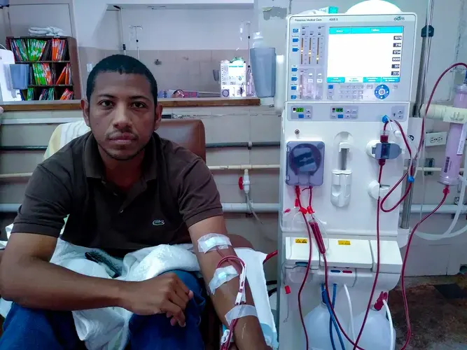 Wearing a brown shirt and a pair of blue jeans, Carlos Román sits down while connected to the dialysis machine at Clinica Riverside, in East Caracas. He receives dialysis three times a week during the morning shift, from 7 a.m. to 11 a.m. Image by Flaviana Sandoval. Venezuela, 2018.