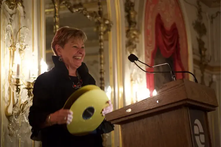 Linda Winslow, former executive producer at PBS NewsHour and current Pulitzer Center board member, holds up a video tape reel from a different era while speaking at the Cosmos Club dinner during the 2019 Washington Weekend celebration. Image by Claire Seaton. United States, 2019.