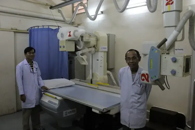 In Sihanouk Hospital Center of HOPE, in Phnom Penh, radiologists pose with one of the hospital's two donated X-ray machines. The hospital is an international charity with a creative operating model: the hospital receives international donations of medicine and equipment, and only charges patients for care that draws on resources that the hospital had to purchase; if diagnosis or treatment is undertaken with donated resources, then the patient isn’t charged. Image by M. G. Zimeta. Cambodia, 2018.