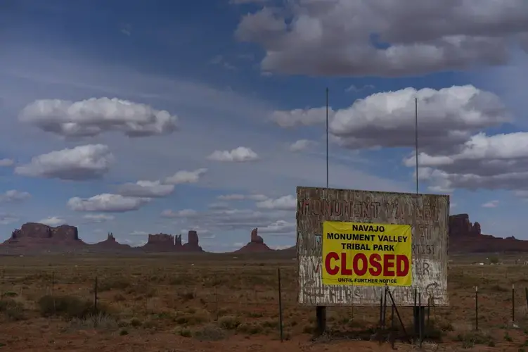 A sign reads 'Navajo Monument Vally Tribal Park Closed Until Further Notice' posted at the entrance of Monument Valley in Oljato-Monument Valley, Utah, on the Navajo reservation April 19, 2020. The reservation has some of the highest rates of coronavirus in the country. If Navajos are susceptible to the virus' spread in part because they are so closely knit, that's also how many believe they will beat it. Image by AP Photo/Carolyn Kaster. United States, 2020.