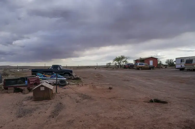 A dog sleeps on the red sand on the end of his chain at the Dinehdeal family compound in Tuba City, Ariz, on the Navajo reservation on April 20, 2020. The Dinehdeal family has been devastated by COVID-19. Image by AP Photo/Carolyn Kaster. United States, 2020.