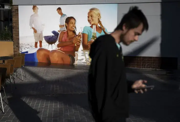 Sam Ware, 22, walks past a billboard while out on a morning walk from the hostel where he is staying at The Entrance, Central Coast, Australia, Thursday, July 25, 2019. Image courtesy of David Goldman. Australia, 2019.