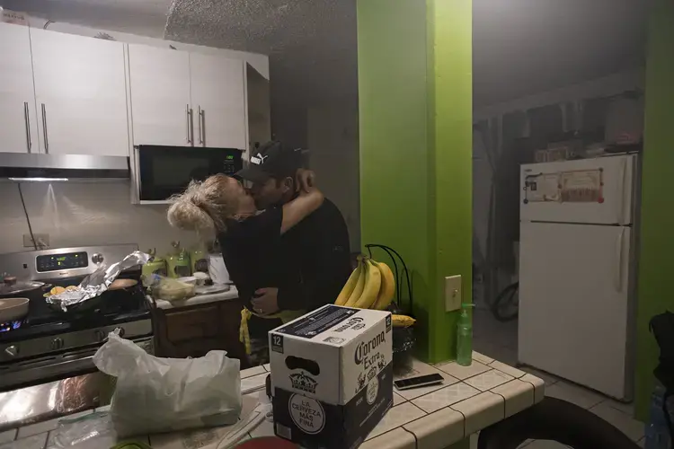 Enedis Flores welcomes home her husband, Ramon, from work as she cooks Thanksgiving dinner at his apartment in Tijuana, Mexico. Ramon, who works as a carpenter, built custom cabinets and painted the walls of the apartment to make it feel more like home for his family. Image by Amanda Cowan. Mexico, 2019.