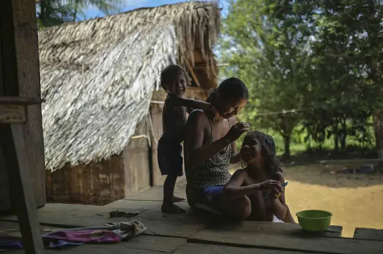 A Timbo Indian mother smiles as she does her six-year-old daughter's hair. Her second son plays behind her. Image by Luis Ángel. Colombia, 2019.