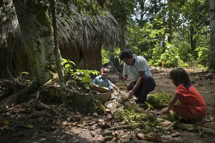 A father cuts up a coconut to share with his two small children. Image by Luis Ángel. Colombia, 2019.