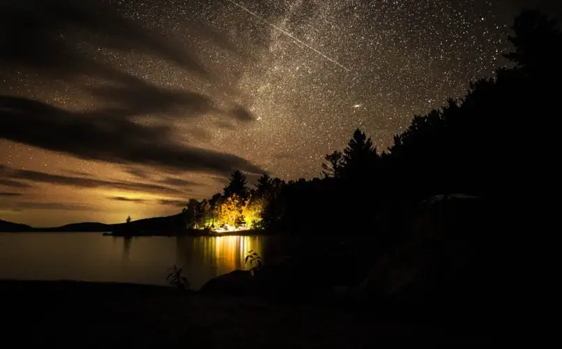 The night sky lights up over the Hanson/Kwan camp at Spencer Lake in T3 R5, in the Unorganized Territories of Maine, on Aug. 3, 2019. Image by Michael G. Seamans. United States, 2019.