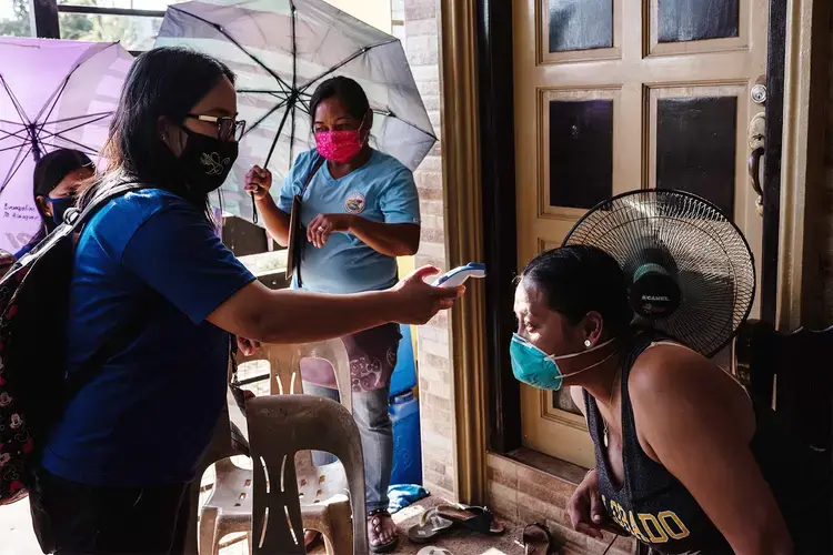 Rosalie Natividad uses a thermometer to check the temperature of Joan Santos, who is under home quarantine. Philippines, 2020.