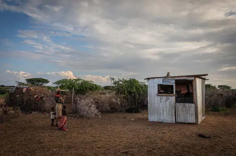 A young mother stands with her children outside a small stall in a village near Laisamis, Kenya. Image by Will Swanson. Kenya, 2020.