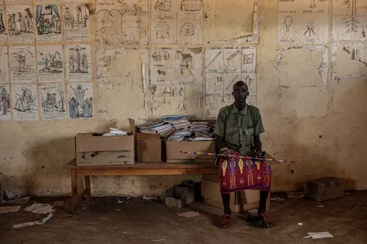A young Rendille moran sits in a shuttered school building near the town of Laisamis in Kenya. Young men broke the windows of the school and have been living in the classrooms since the school was closed due to the COVID-19 pandemic. Image by Will Swanson. Kenya, 2020.