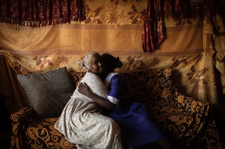 Dorcas Choya sits with Susie on her couch, who fled her home when her parents brought a circumciser to cut her. “When I saw her I just ran,” said Susie. “I didn’t bother taking anything. I ran without shoes.' Image by Will Swanson. Kenya, 2020.