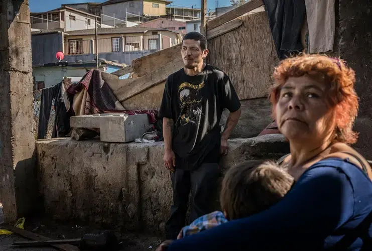 Estel, a grandmother, cradles a grandchild in the garden of her home that touches the old border wall. Her son-in-law, Jesus, was deported from the United States because of a felony conviction. He now dreams of getting a visa to Canada. Image by James Whitlow Delano. Mexico, 2017.