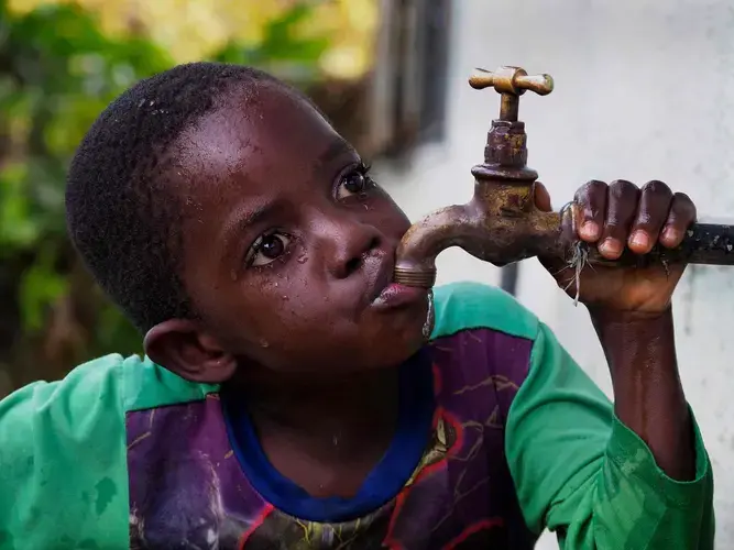 Lead poisoning victim Gift Phiri, 6, drinks in his backyard in Chowa, the heavily polluted township next to the closed lead mine. Image by Larry C. Price. Zambia, 2017.