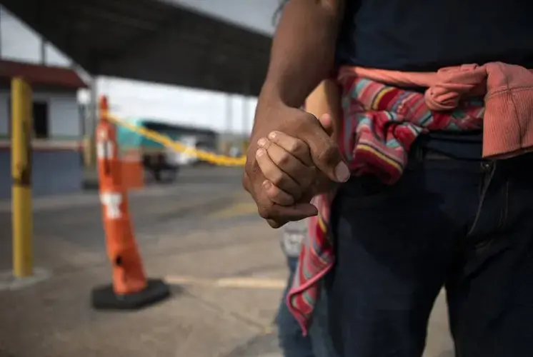 A Honduran migrant holds his daughter's hand at an immigration checkpoint in Nuevo Laredo. The pair requested asylum in the United States but were returned to Mexico to await their case. The father was uncertain whether they would remain in Mexico until their court date. Image by Miguel Gutierrez. United States, 2019.