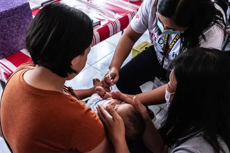 Rosalie Natividad administers a vaccine to a baby in a clinic. Image by Xyza Cruz Bacani. Philippines, 2020.