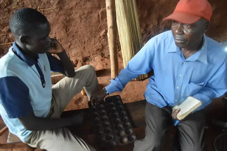 Two men of Bukaleba village playing a local game. The village chairman Ongom said the salaries received by Bukaleba residents for casual labor in the forest can barely provide for their basic needs. Image by Annika McGinnis. Uganda, 2019.