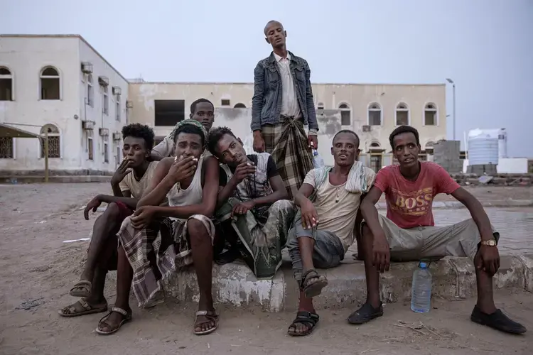Ethiopian migrants sit together and smoke, as they take shelter in the '22nd May Soccer Stadium,' destroyed by war, in Aden, Yemen. Image by AP Photo/Nariman El-Mofty.
