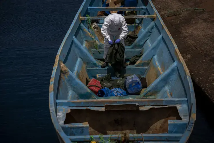 A police officer inspects a boat where 15 Malians were found dead adrift in the Atlantic on Thursday, Aug. 20, 2020, in Gran Canaria island, Spain. Image by Emilio Morenatti/AP Photo. Spain, 2020.