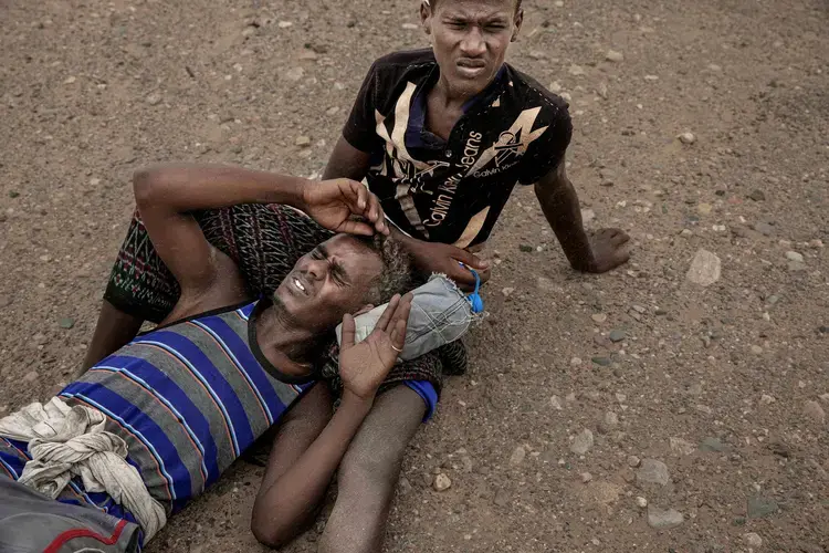 Ethiopian migrants lie on the ground because of a sandstorm in Lahj, Yemen. Image by AP Photo/Nariman El-Mofty. Yemen, 2020.