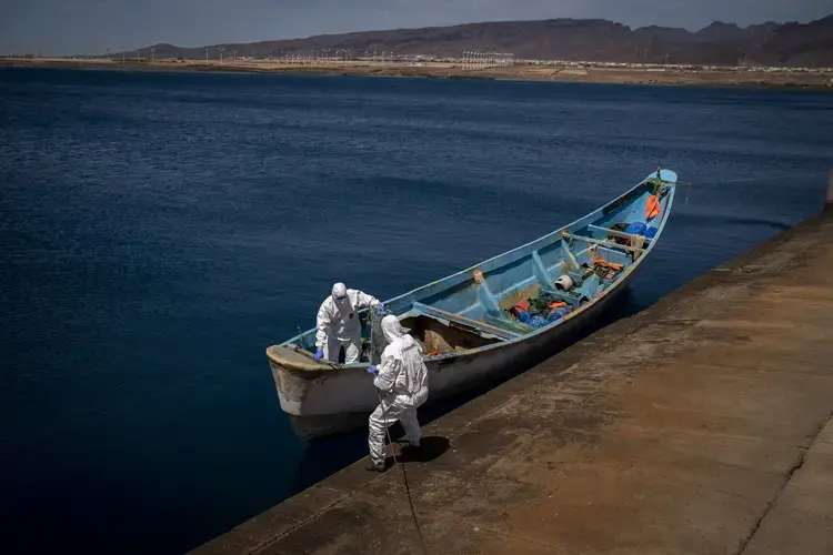 Police officers inspect a boat where 15 Malians were found dead adrift in the Atlantic on Thursday, Aug. 20, 2020, in Gran Canaria island, Spain. Image by Emilio Morenatti/AP Photo. Spain, 2020.