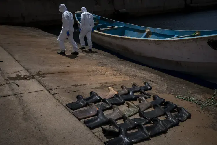 Waterproof boots are placed on the ground by police officers as they inspect a boat where 15 Malians were found dead adrift in the Atlantic on Thursday, Aug. 20, 2020, in Gran Canaria island, Spain. Image by Emilio Morenatti/AP Photo. Spain, 2020.jpeg