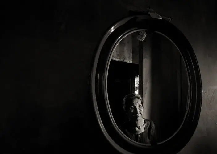 Emilia dela Cruz Mangilit is reflected in a mirror in her home in the village of Mapaniqui. Mangilit was only 15 years old when her village was shelled, then attacked by the Japanese during World War II. Image by Cheryl Diaz Meyer. Philippines, 2019.