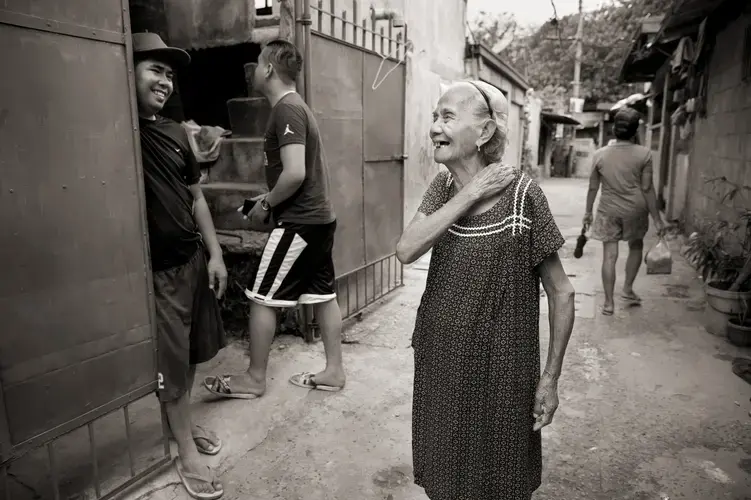 Narcisa Claveria laughs with neighbors in this 2019 photo. Even in the coronavirus pandemic, she goes out, wearing a mask. 'I'd rather die in the streets,' she says, 'than stay dying of sadness at home.' Image by Cheryl Diaz Meyer. Philippines, 2019.