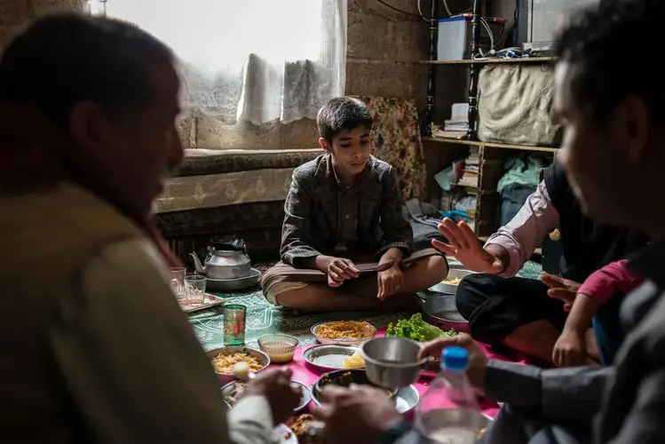 Salah (center) has lunch with his father, Yahya, and their family. Image by Alex Potter. Yemen, 2018.