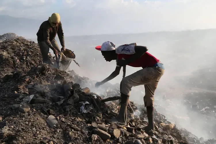 At the city landfill, men look for metal near the edge of a pit that used to be full of raw sewage. Construction delays at the Titanyen sewage treatment plant meant that raw sewage continued to be dumped at the landfill for months after the cholera epidemic began in 2010. Image by Marie Arago/NPR. Haiti, 2017.