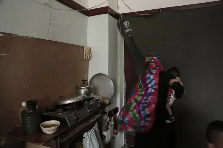 A woman holds her baby as she leaves her room in a shelter for displaced persons in Ibb. Image by Nariman El-Mofty/AP Photo. Yemen, 2018. 