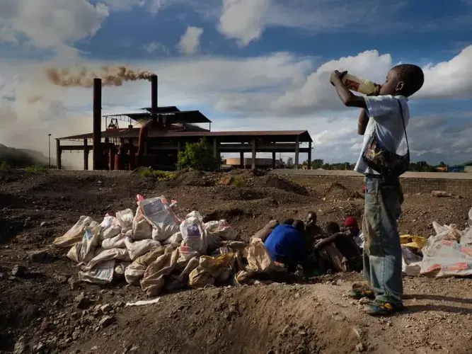 14-year-old Brian Jovo pauses for a drink of water he had just collected from a small pond at the base of Black Mountain. Soil in the area contains hundreds of times the U.S. EPA's safe environmental lead levels. Brian and other men and boys work in direct contact with the contaminated soil. Image by Larry C. Price. Zambia, 2017.