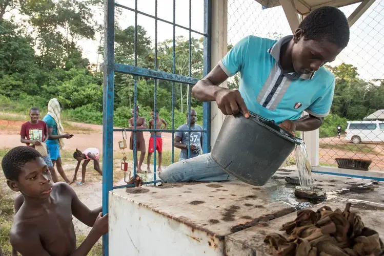 Children watch as Prika Riandro, 17, fills up a gas generator to power a few hours of electricity for his village on Wednesday, March 15, 2017 in Adjuma Kondre, Suriname. Like many villages in the country, Adjuma Kondre relies on an inconsistent government supply of fuel to supply electricity for a few hours per day. Image by Stephanie Strasburg.
