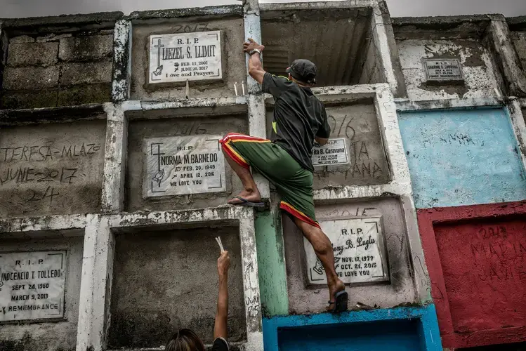 Liezel’s father, Cerlon Llimit, climbs up to her tomb at the cemetery to light candles for his daughter. Image by James Whitlow Delano. Philippines, 2017.