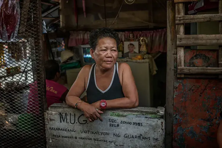 Rosita Opiasa, 59, runs this corner shop in Market 3 shanty town, an area of Navotas. Her son, Jayson Rivera, 32, was killed in the drug war. (His photo can be seen in the background.) Opiasa still supports President Duterte, which is rare in Market 3. From her shop, she sells single cigarettes and small bottles of shampoo and detergent because her customers can’t afford larger sizes. Image by James Whitlow Delano. Philippines, 2017.