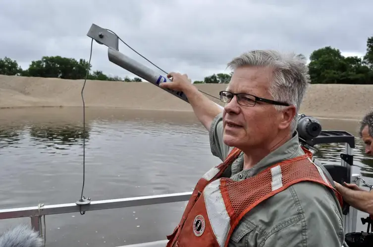 Jon Hendrickson of the Army Corps of Engineers stands in a boat near piles of dredged Mississippi River sediment on Crater Island, Wisconsin. Image by Tristan Baurick / NOLA.com | The Times-Picayune. United States, 2019.<br />